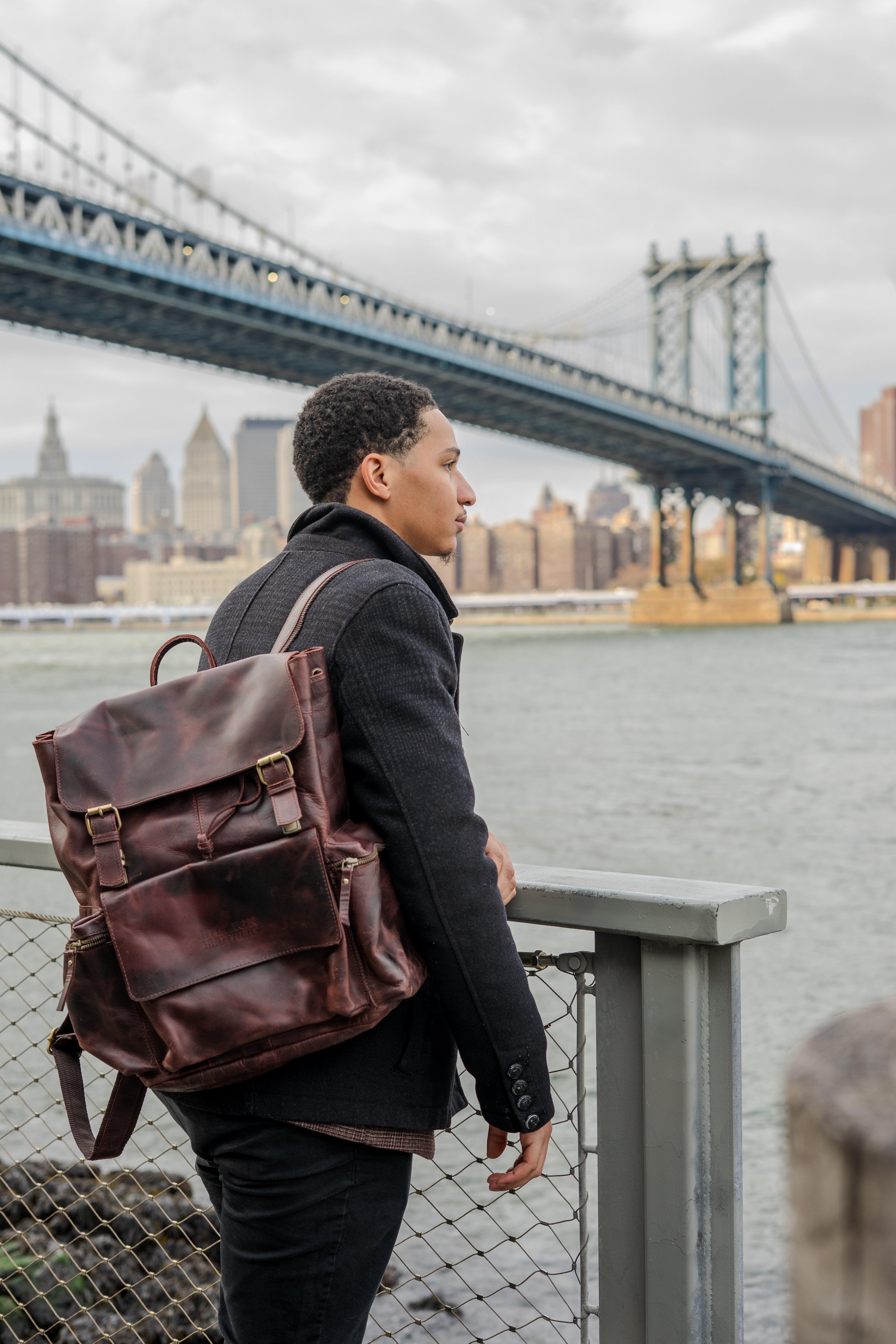 Person wearing a brown leather backpack with a cityscape and bridge in the background