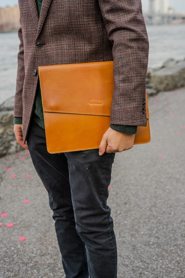 Person holding a brown leather briefcase by a waterfront